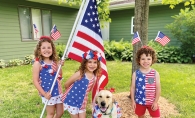Kids decked out in patriotic clothing pose with the American flag and a dog.