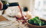 A glass of red wine is poured at a dinner table.