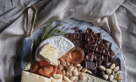 A plate full of various chocolates, cheese, fruits and snacks.