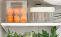 Plastic containers filled with food sit on the shelves of a well-organized fridge.