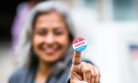 A member of the League of Women Voters holds up an "I Voted" sticker.