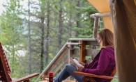 A woman reads a copy of Of Bears and Ballots at a cabin.