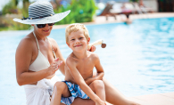 A woman applies sunscreen to her young son's back.