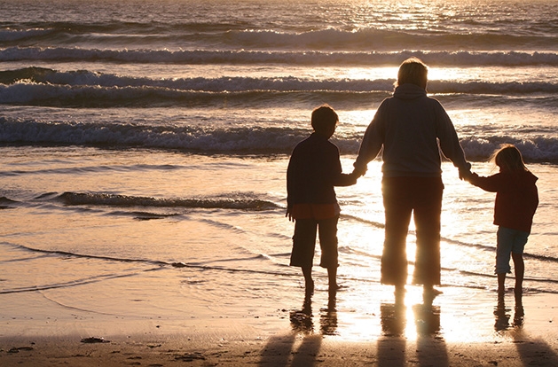 A mother holds hands with her children on a beach.