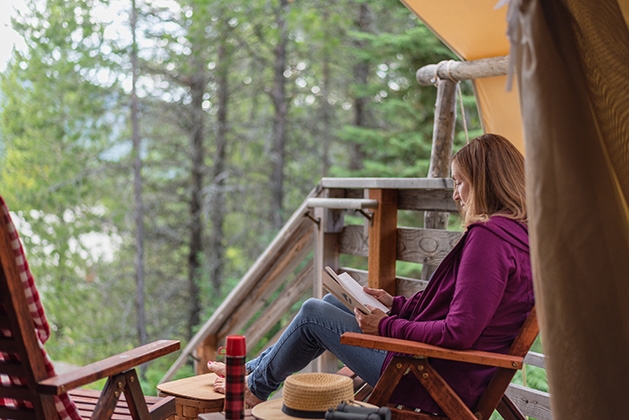 A woman reads a copy of Of Bears and Ballots at a cabin.