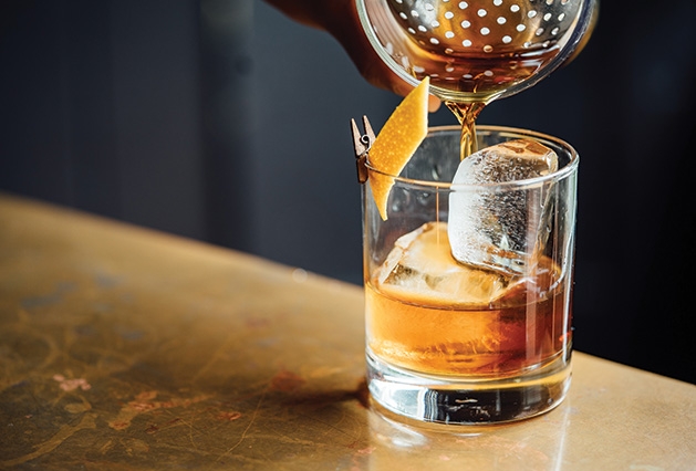 A bartender pours an old fashioned into a glass.