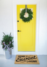 A yellow door decorated with a wreath on a home ready for a holiday sale.