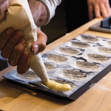 Piping madeleine cookies into a prepared baking sheet.