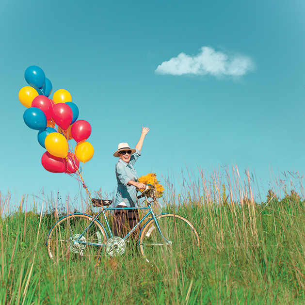 A woman bikes in a field with a bundle of balloons in a shot from See Them Shine