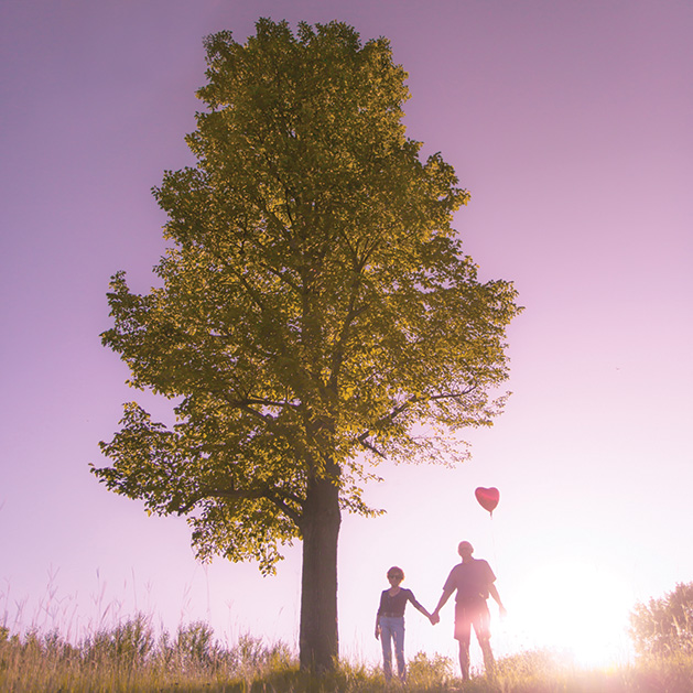 Two people stand near a tree, one of them holding a heart balloon, in a shot from See Them Shine