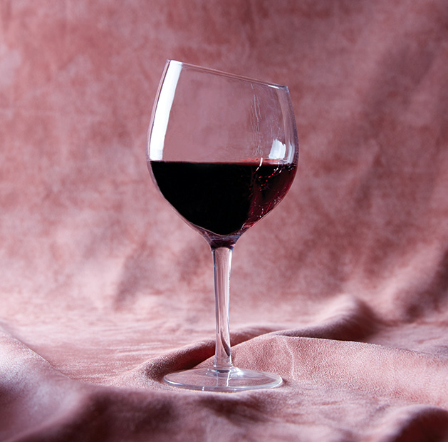 A glass of red wine sits on a pink satin sheet
