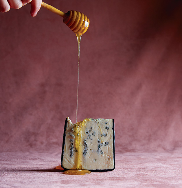 Someone drips honey onto a chunk of cheese.