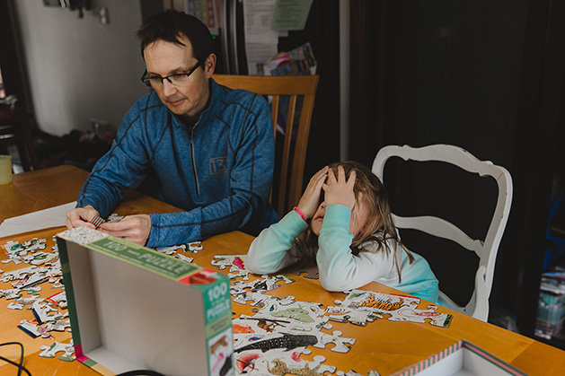 A dad and his daughter work on a puzzle together.