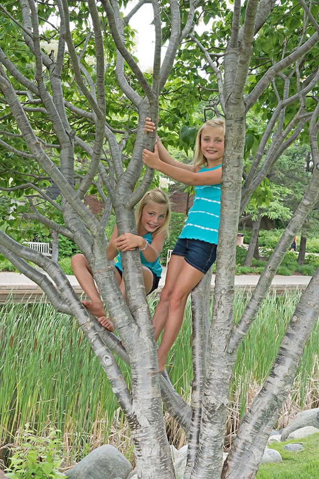 Two girls pose while climbing a tree.