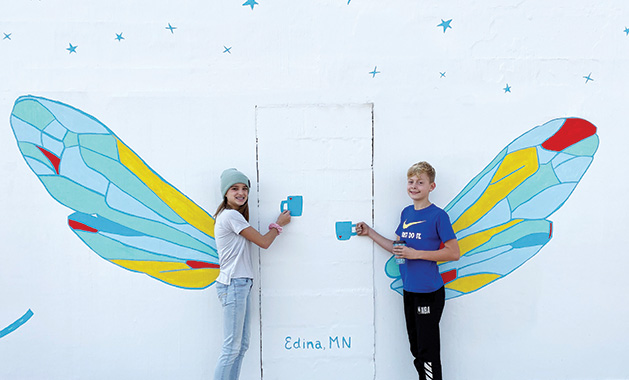 Two kids pose in front of the mural painted on the side of the Vernon Avenue Caribou Coffee in Edina