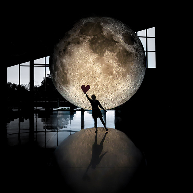 A person holds a paper heart in front of the moon in one of the shots from See Them Shine